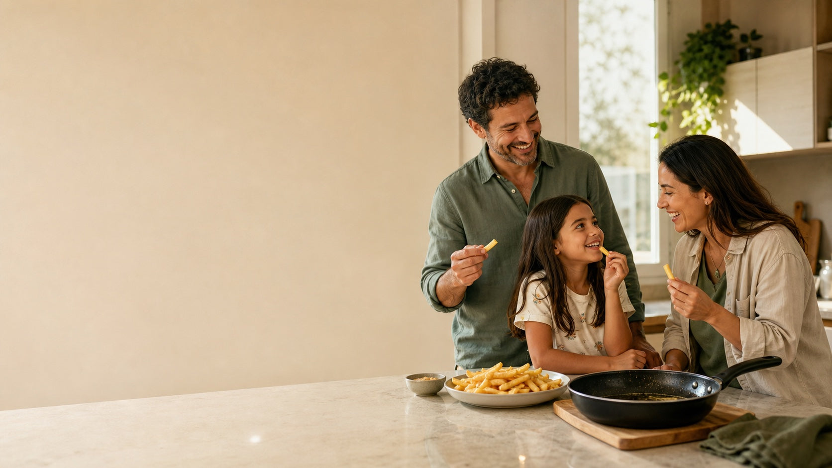 Familia compartiendo papas fritas en una cocina cálida, con la sartén ya utilizada sobre el mesón